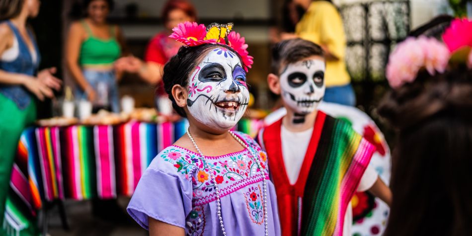 Children with painted skull faces at a festive Día de los Muertos gathering.